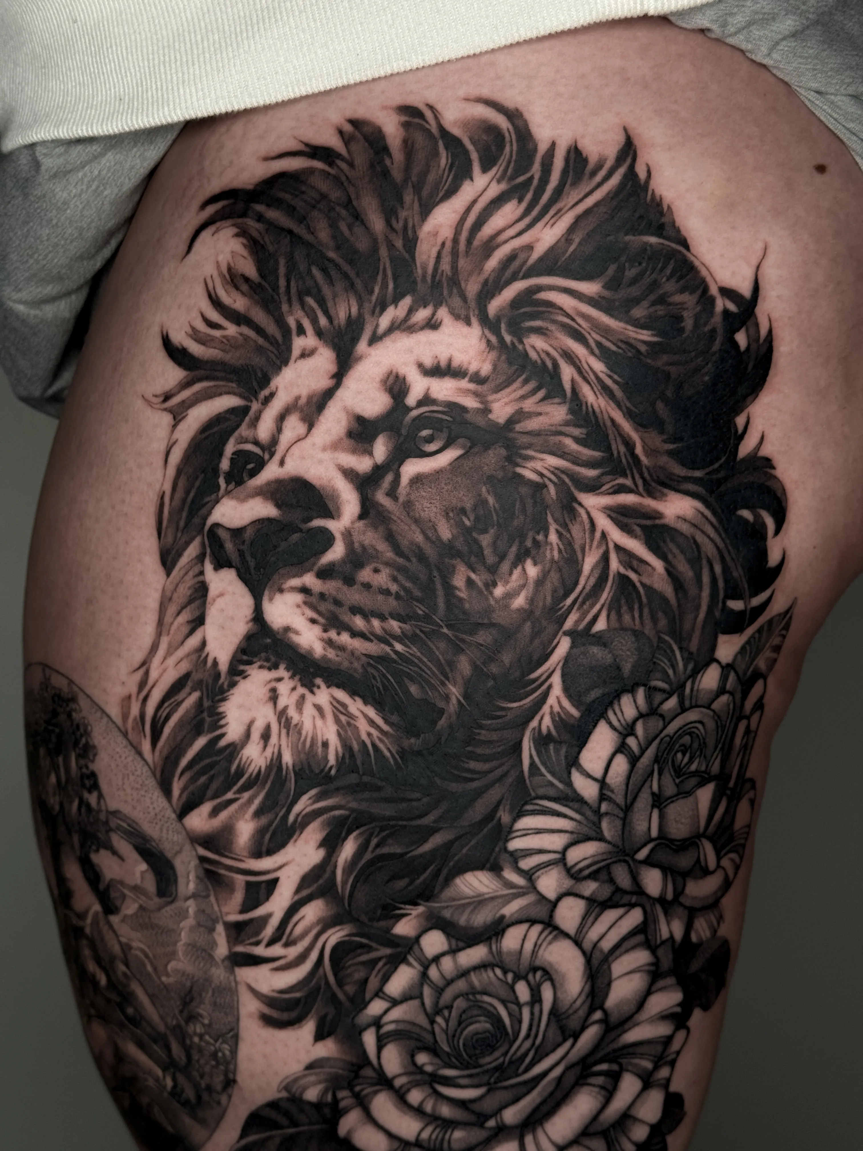 Black and gray realism tattoo of a lion with roses on the thigh