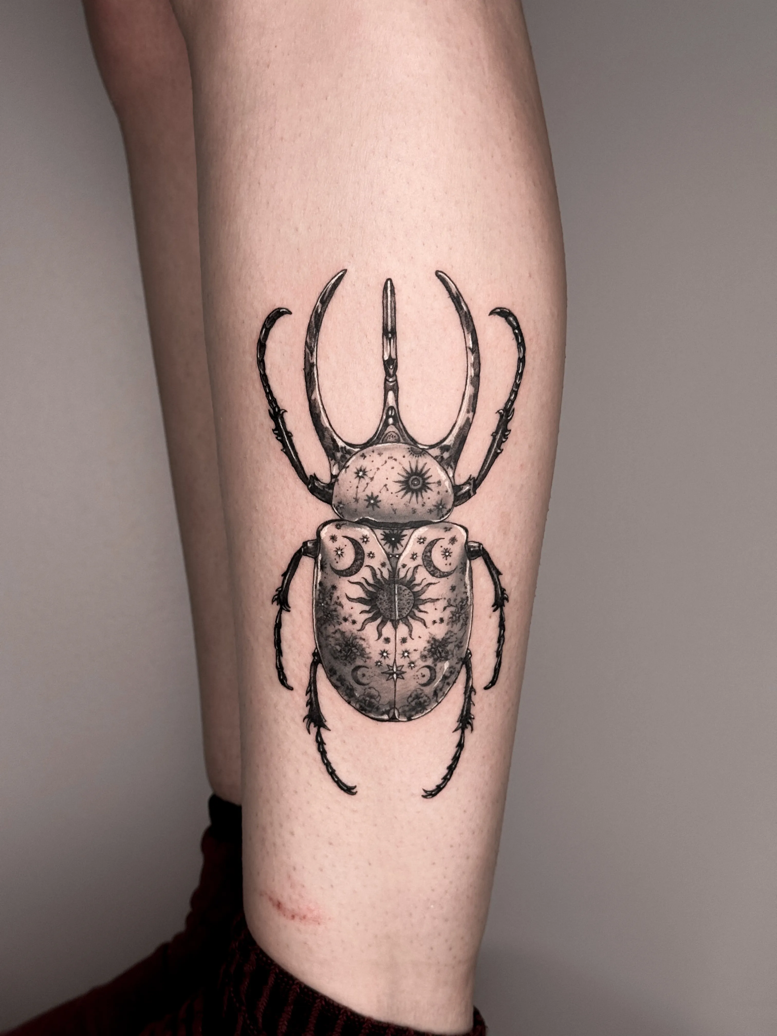 Black and gray tattoo of a celestial scarab beetle on the leg