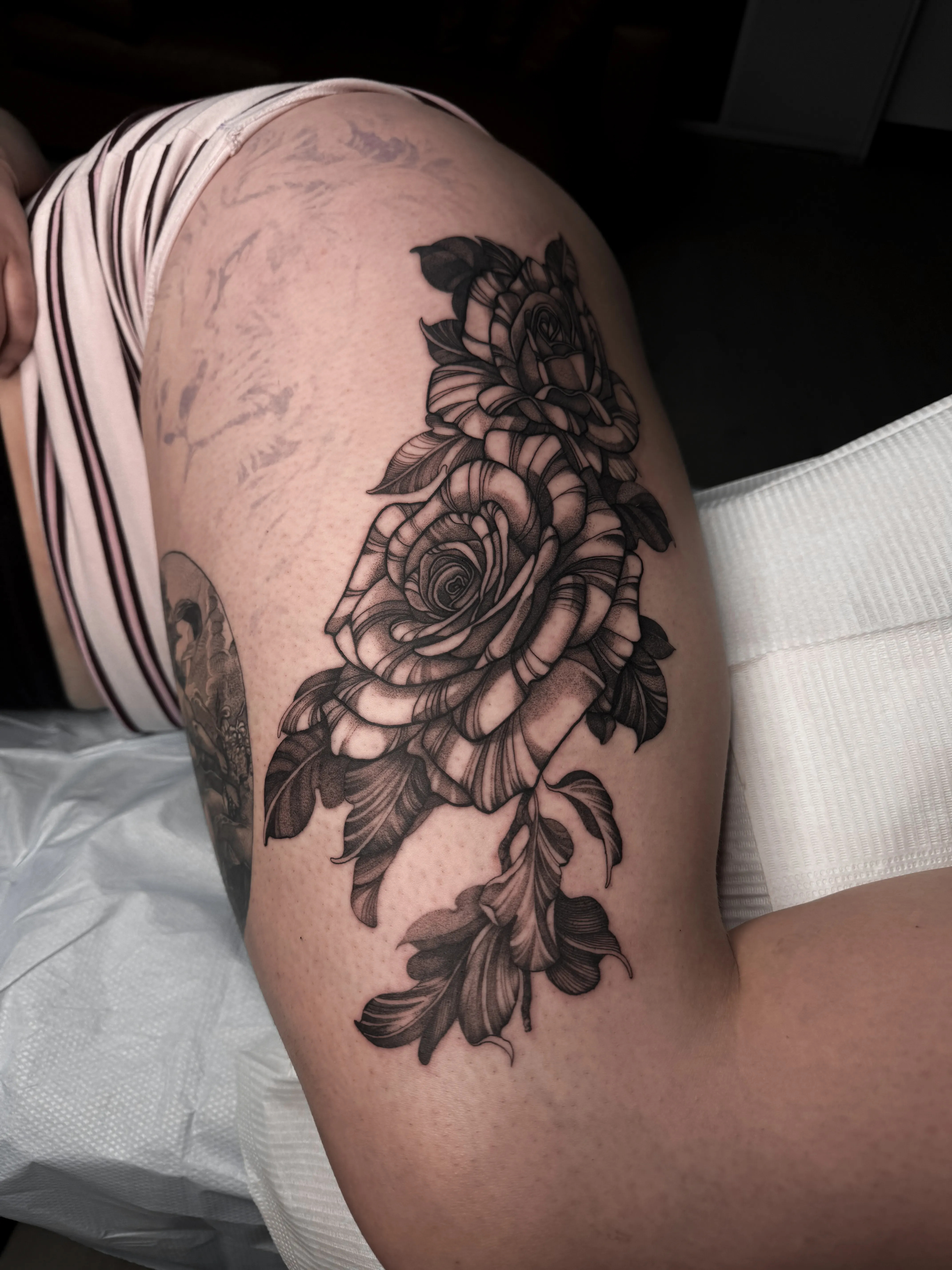 Black and gray floral tattoo of two large roses with trailing leaves on the thigh
